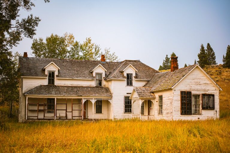 Older white and brown house beside a grass field, the kind of property beginners analyze on a first wholesale deal