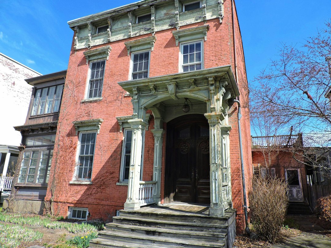 Older red brick house with a vintage porch, typical of homes moving through the New York foreclosure process